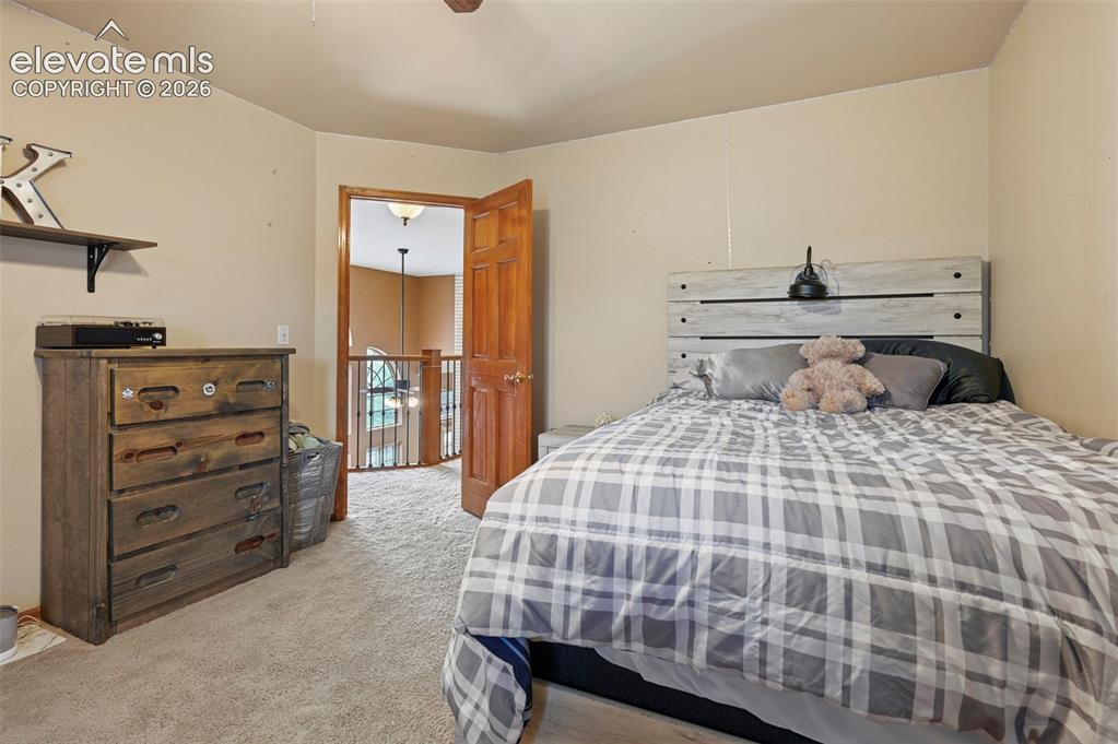 Image 27 of 50: Second floor bedroom with carpeted flooring, wood-finish door, and light-to