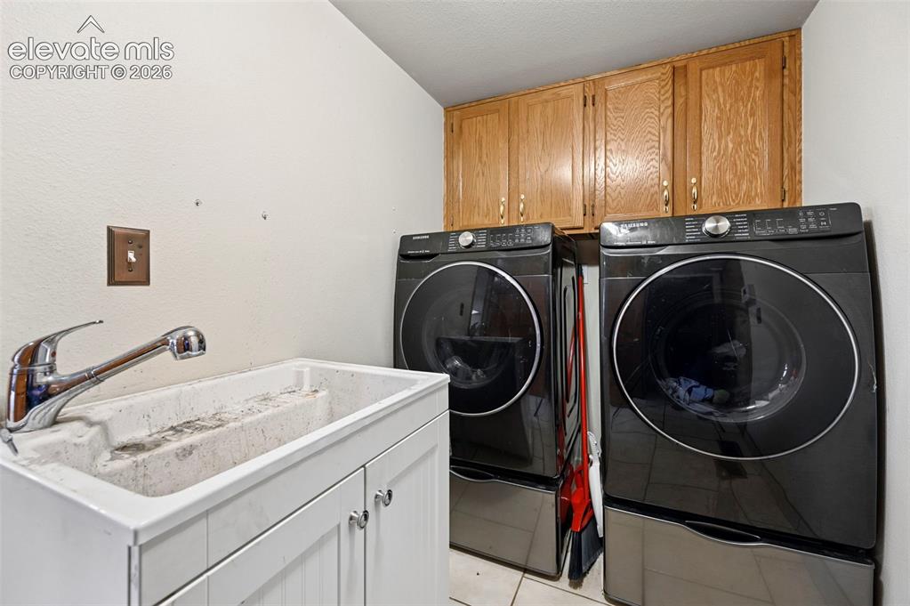 Image 38 of 50: Utility sink with chrome faucet, white cabinetry, and overhead wood-finish