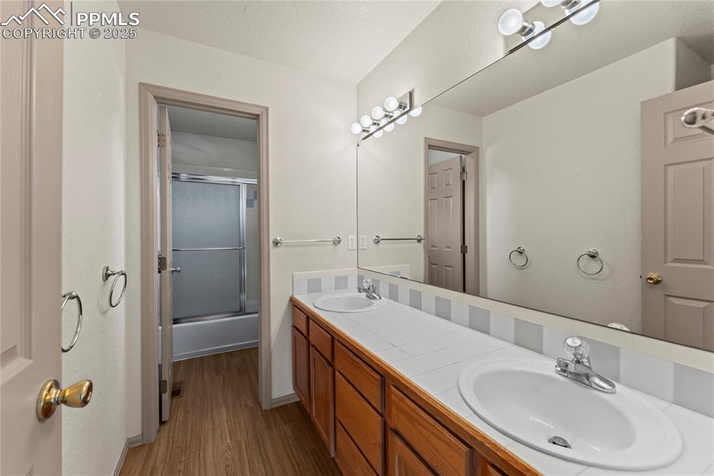 Image 26 of 38: Master 
Bathroom with wood finished floors, double vanity, and enclosed tu