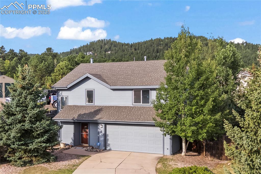 Image 3 of 38: Traditional home with a view of trees, roof with shingles, driveway, and a 