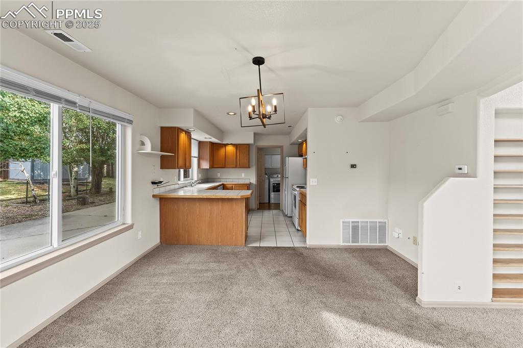 Image 8 of 38: Kitchen with light carpet, brown cabinetry, a chandelier, a peninsula, and 