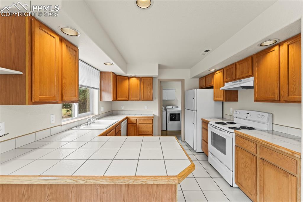 Image 9 of 38: Kitchen with white appliances, tile countertops, recessed lighting, light t