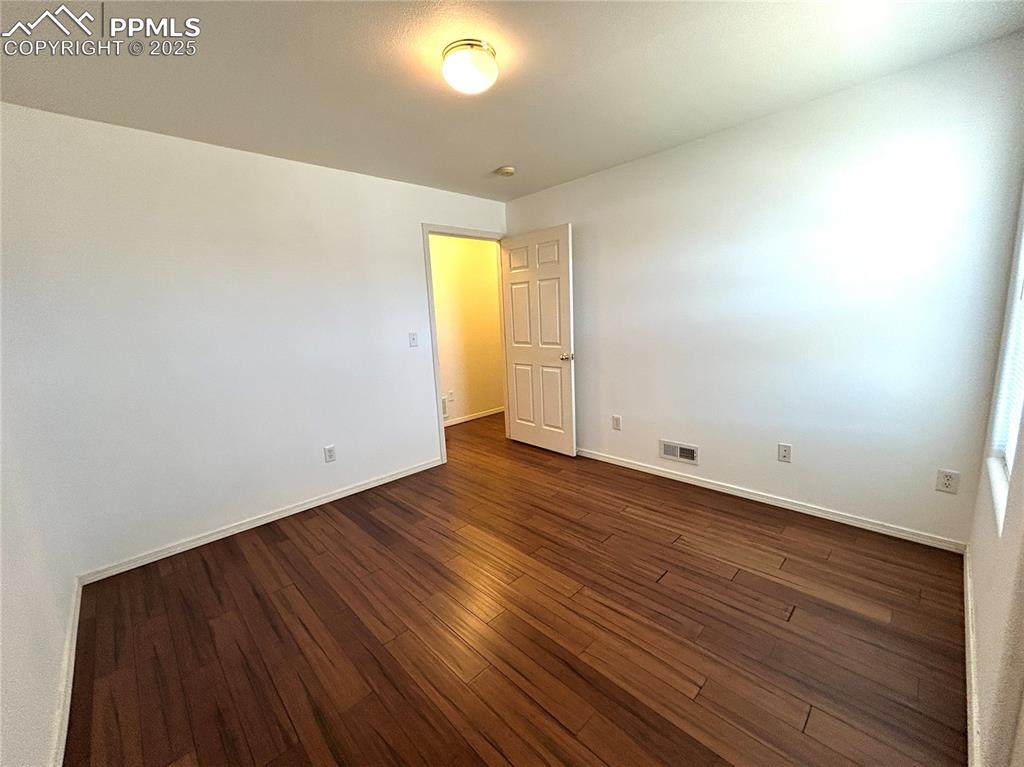 Image 23 of 43: Empty room with dark wood-style flooring, baseboards, and visible vents
