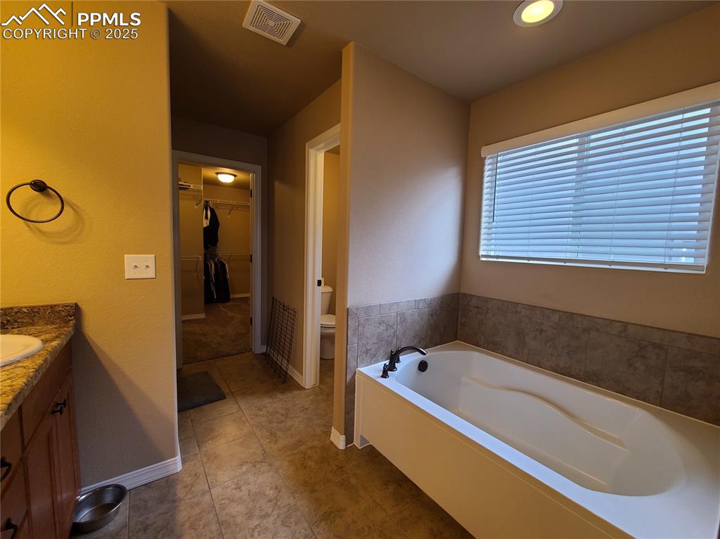 Image 17 of 29: Full bathroom with vanity, a bath, a spacious closet, and dark tile pattern