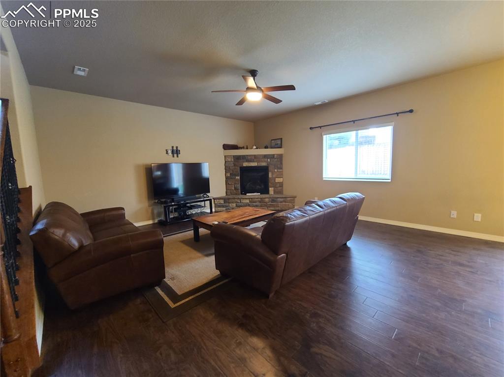 Image 8 of 29: Living area with a fireplace, dark wood-style flooring, and ceiling fan