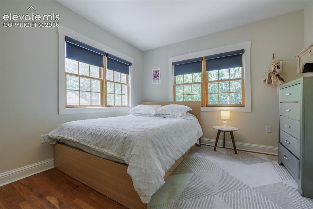 Image 17 of 49: Bedroom featuring wood-finish flooring, two large windows with trim, and ne