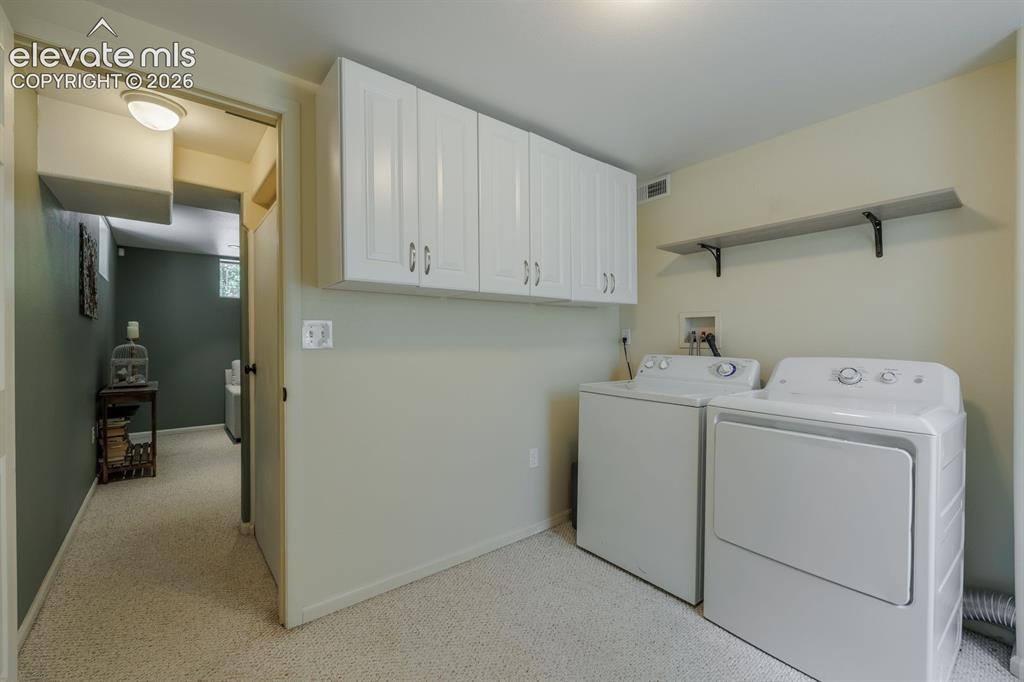 Image 33 of 49: Laundry area featuring white cabinetry, a floating shelf, and neutral wall