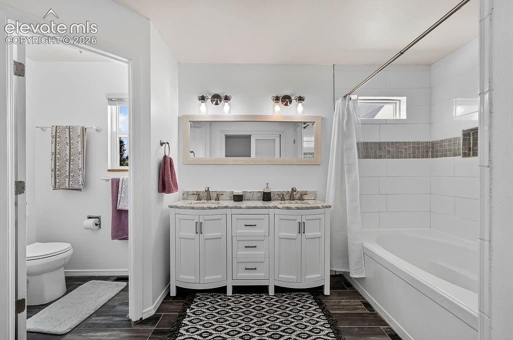 Image 22 of 30: Dual vanity with stone countertop, tile flooring, and a shower-tub combinat