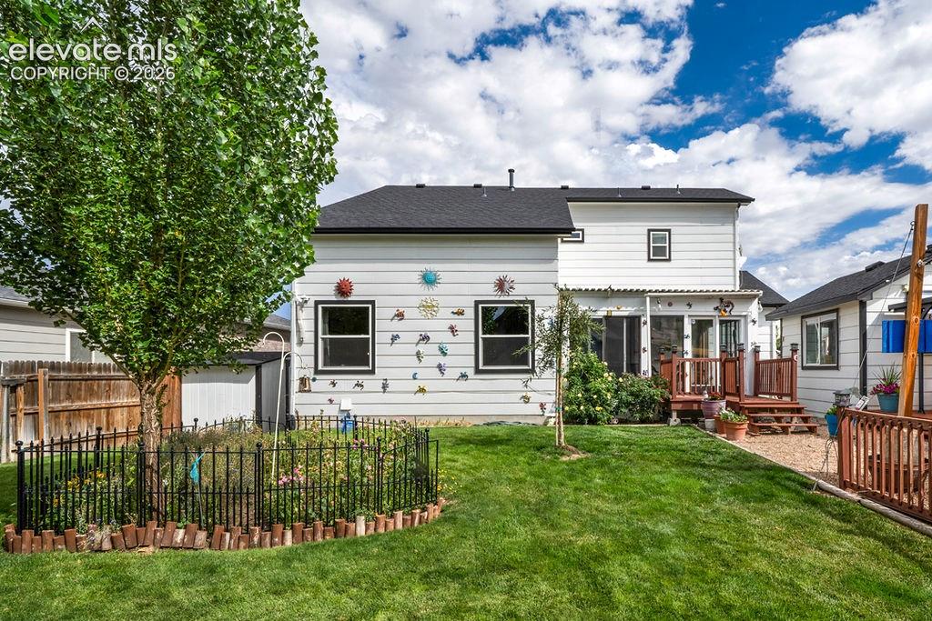 Image 29 of 30: Expansive backyard featuring a green lawn, established tree, and a garden b