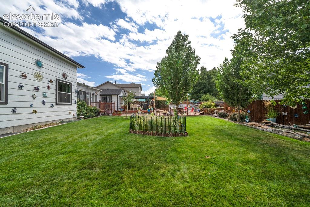 Image 3 of 30: Expansive green lawn, mature trees, wood privacy fencing, and a built-in de