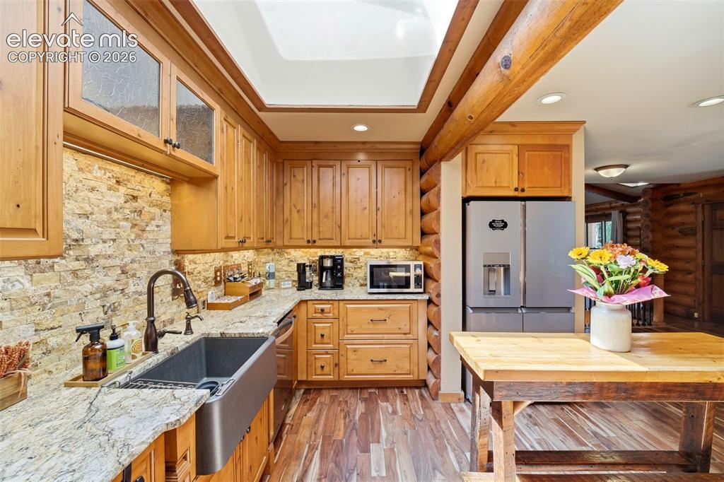 Image 12 of 49: Kitchen featuring wood cabinetry, stone backsplash, stainless steel farmhou