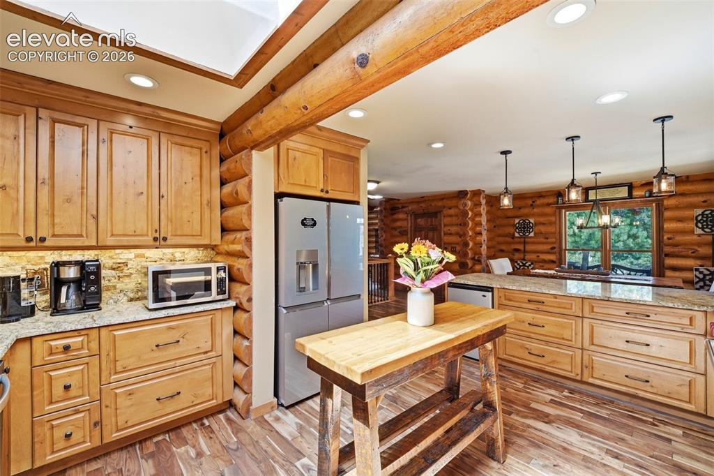 Image 13 of 49: Kitchen featuring log-style walls, wood-finish flooring, and light wood cab
