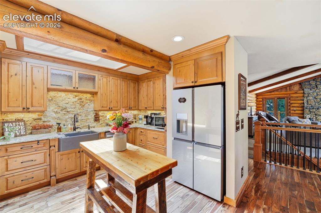 Image 14 of 49: Kitchen featuring natural wood cabinetry, stone backsplash, light-toned cou
