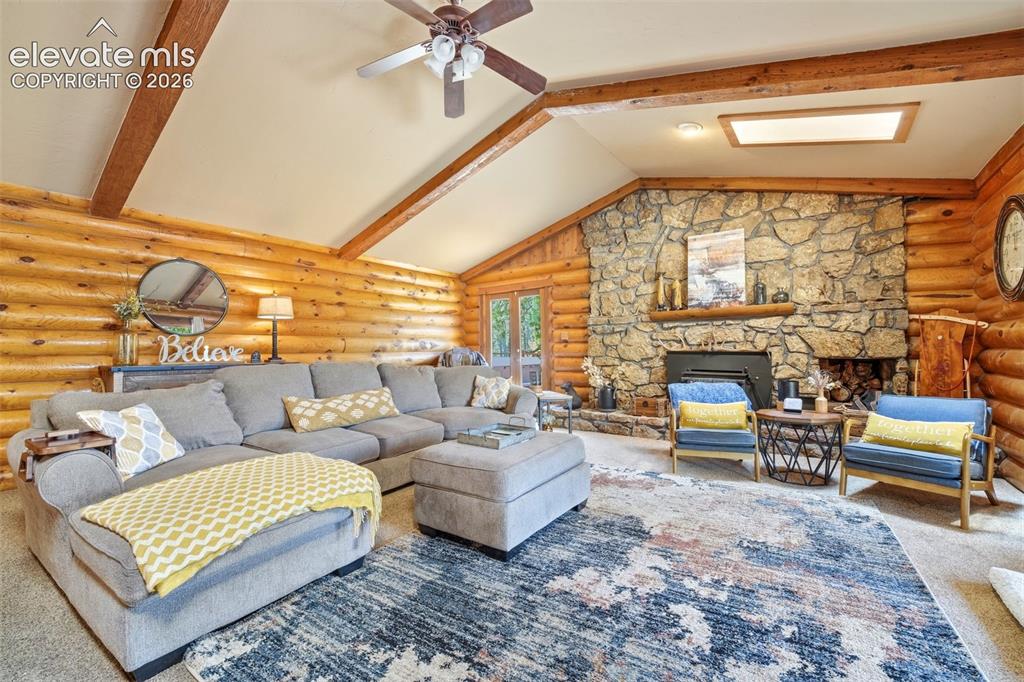 Image 17 of 49: Spacious living area featuring log walls, a stone fireplace, vaulted ceilin