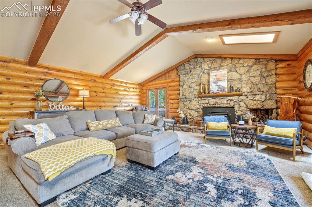 Image 18 of 50: Spacious living area featuring log walls, a stone fireplace, vaulted ceilin