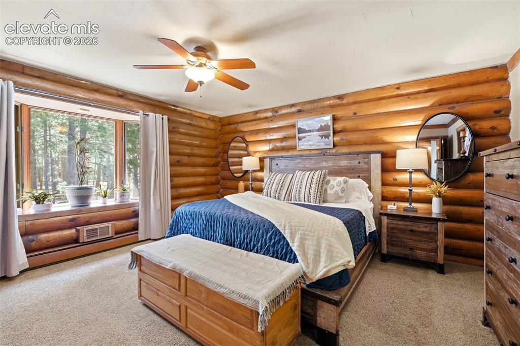 Image 18 of 49: Bedroom featuring natural wood log walls, a large bay window, ceiling fan w