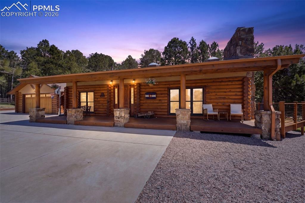 Image 2 of 49: Log cabin exterior featuring a covered porch, stone-wrapped columns, and a