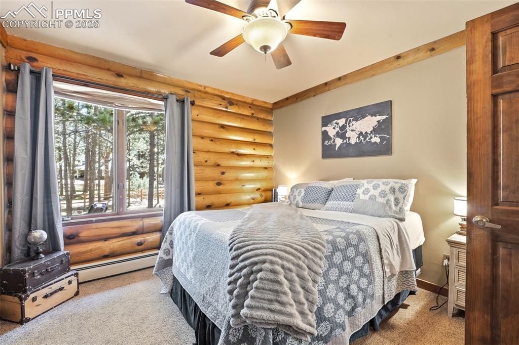 Image 26 of 50: Bedroom featuring log walls, a ceiling fan with light fixture, a window wit
