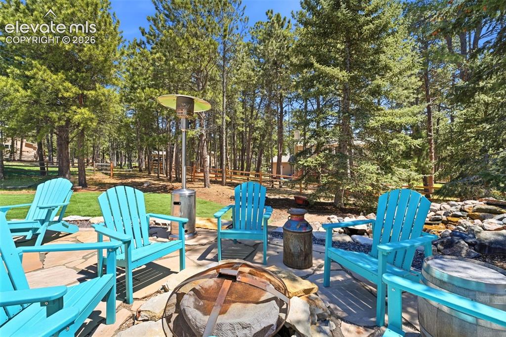 Image 38 of 49: Stone patio featuring a fire pit, surrounded by mature trees