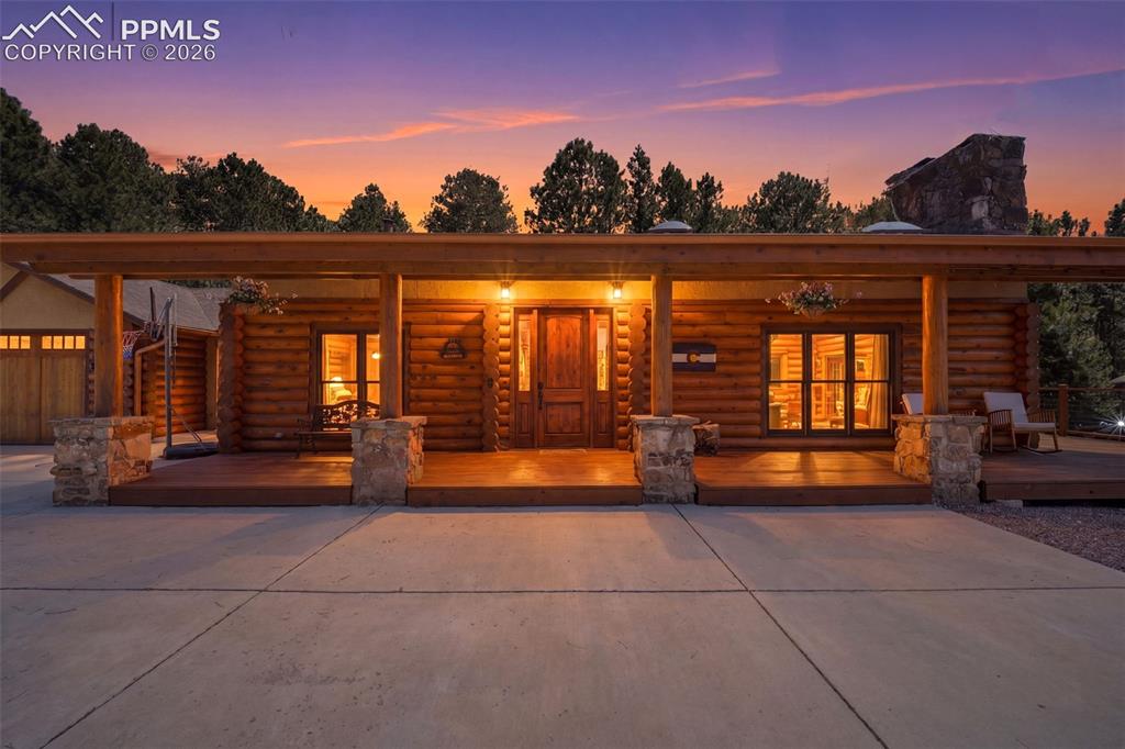 Image 4 of 49: Log cabin exterior featuring a covered porch with stone columns, a solid wo