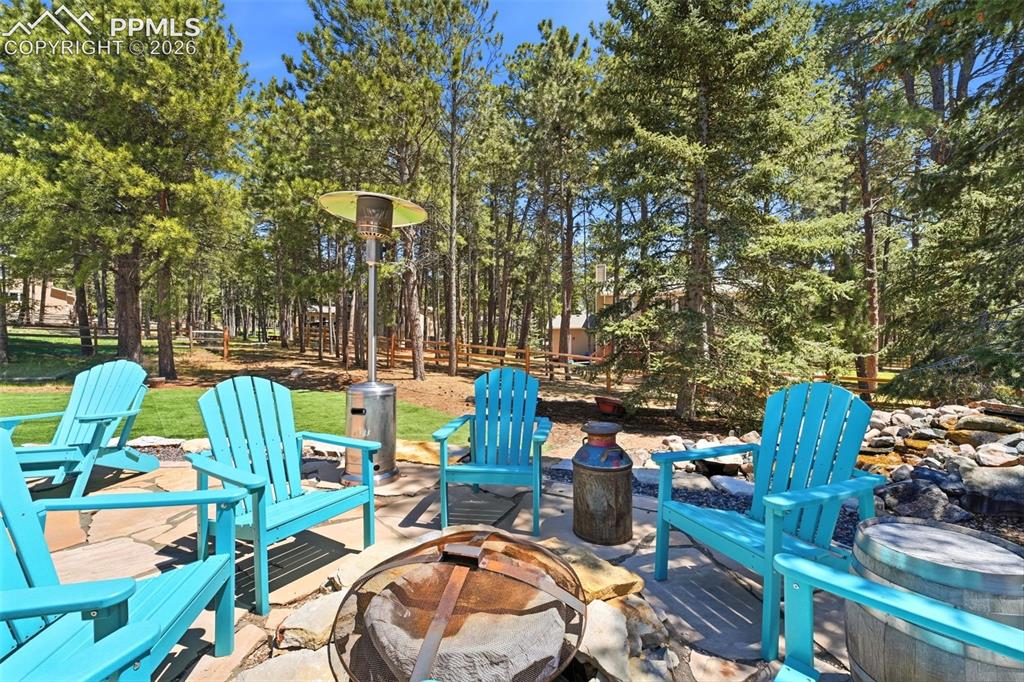 Image 40 of 50: Stone patio featuring a fire pit, surrounded by mature trees