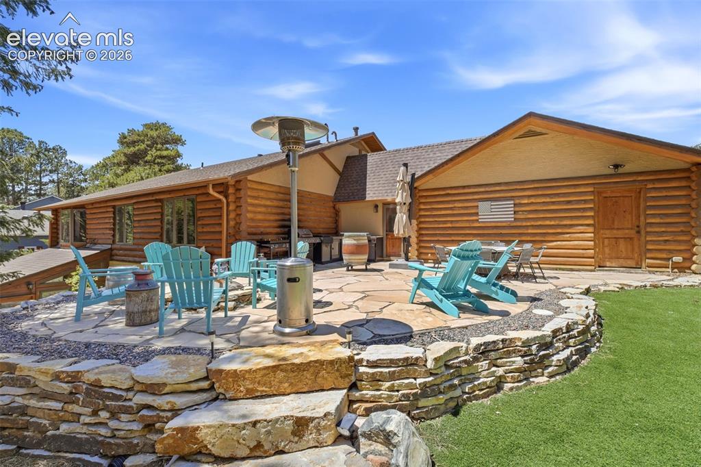 Image 40 of 49: Flagstone patio with a stone retaining wall, artificial turf, and a log cab