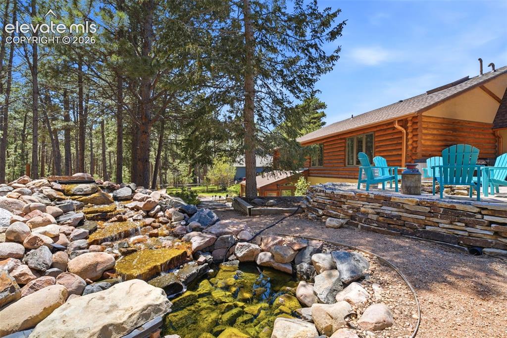 Image 41 of 49: Outdoor patio with a stone retaining wall and a rock-lined water feature