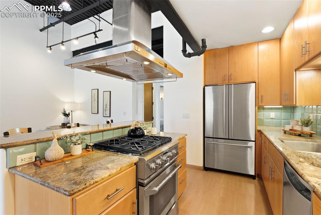 Image 12 of 38: Kitchen with stone counters, stainless steel appliances, an island with a g