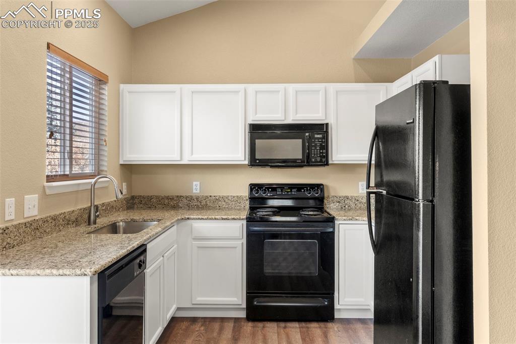 Image 10 of 25: Kitchen featuring black appliances, light stone counters, white cabinetry, 