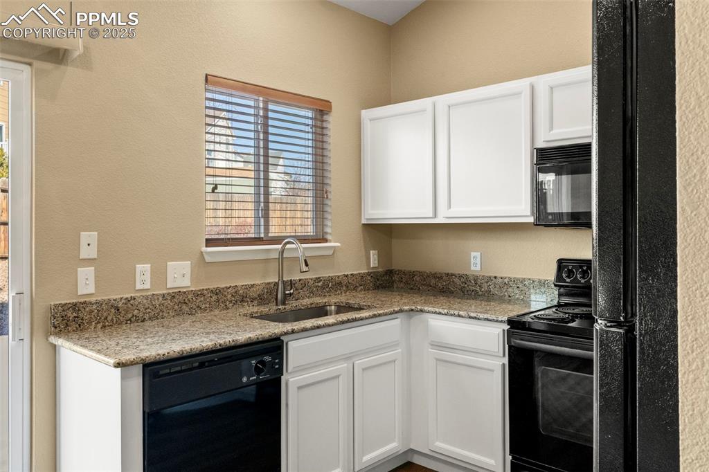 Image 11 of 25: Kitchen with black appliances, light stone countertops, white cabinetry, an