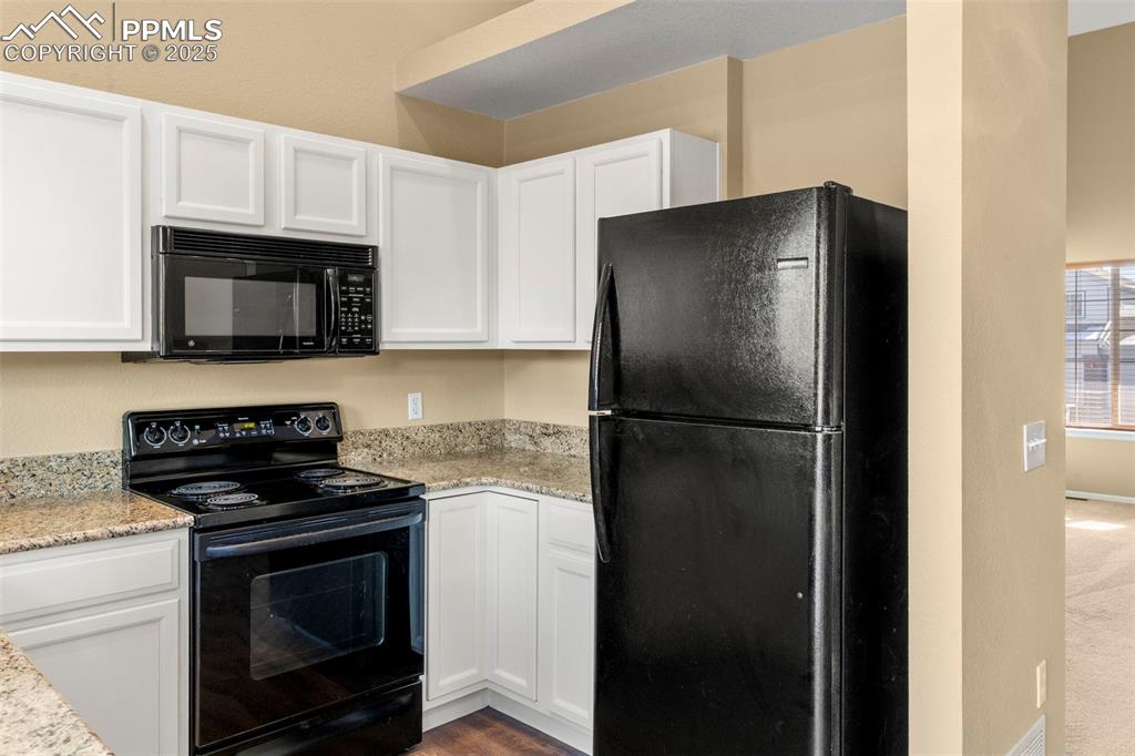 Image 12 of 25: Kitchen featuring black appliances, white cabinets, and light stone counter
