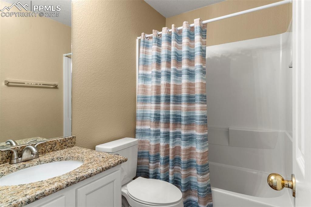 Image 19 of 25: Bathroom featuring a textured wall, shower / tub combo with curtain, and va