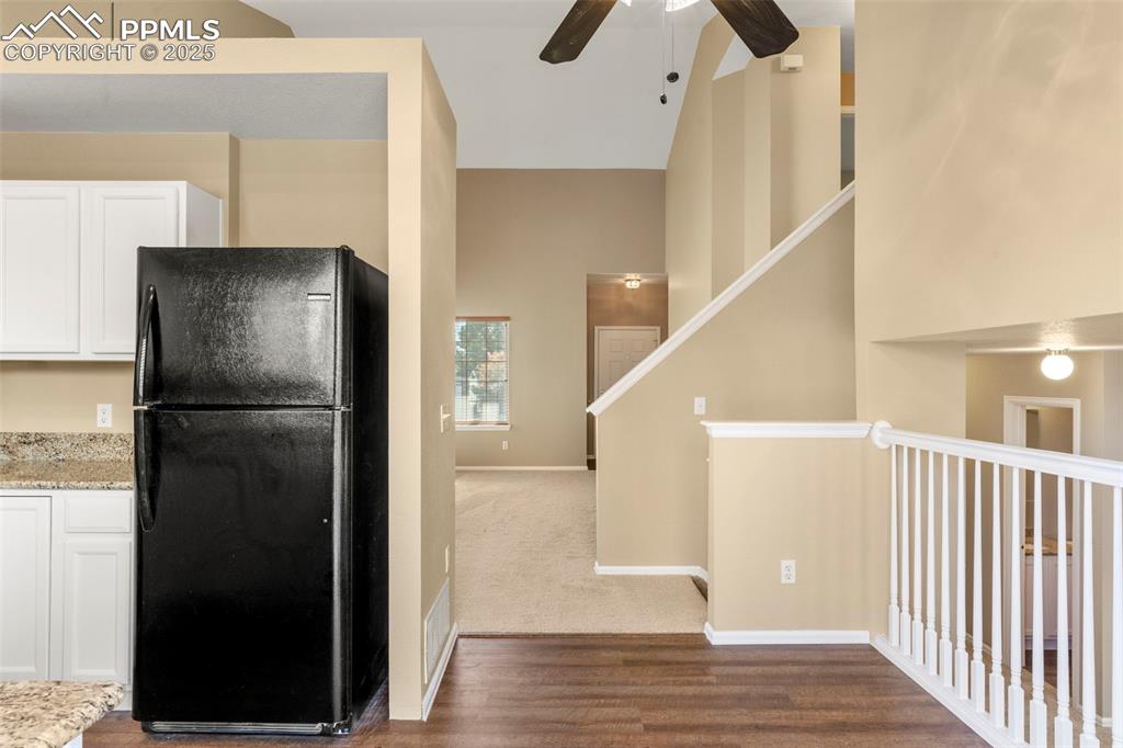 Image 9 of 25: Kitchen with freestanding refrigerator, white cabinetry, high vaulted ceili