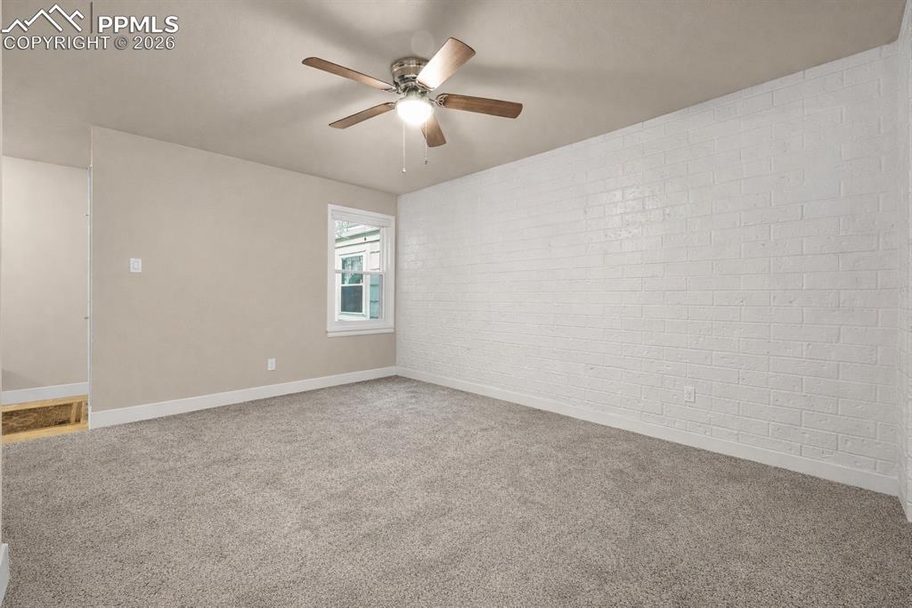 Image 4 of 21: Spare room featuring brick wall, light carpet, and ceiling fan