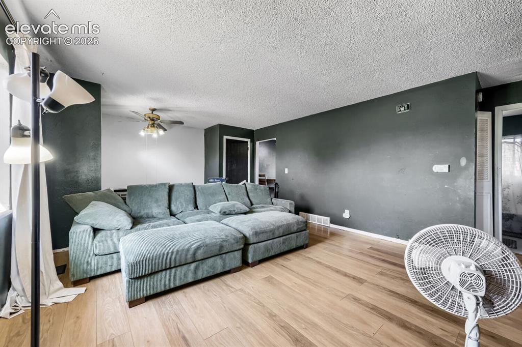 Image 4 of 17: Spacious living area featuring wood-finish flooring, a ceiling fan, and amp