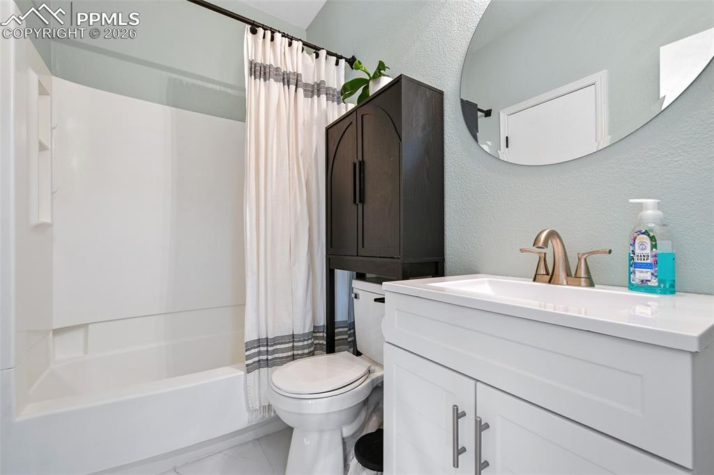 Image 13 of 27: Bathroom featuring a textured wall, vanity, and shower / tub combo with cur