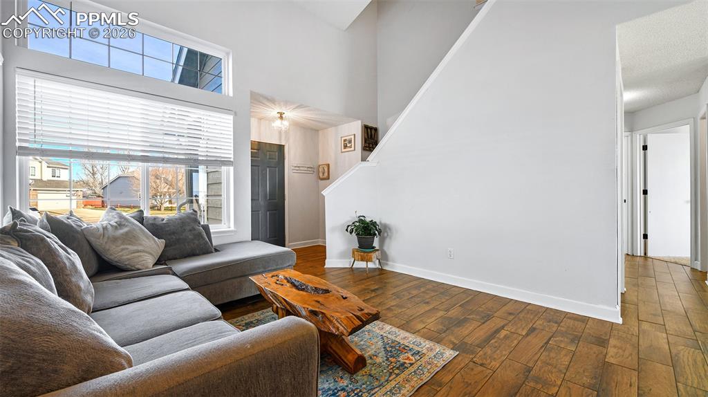 Image 4 of 27: Living room featuring dark wood-style floors, a high ceiling, and stairs