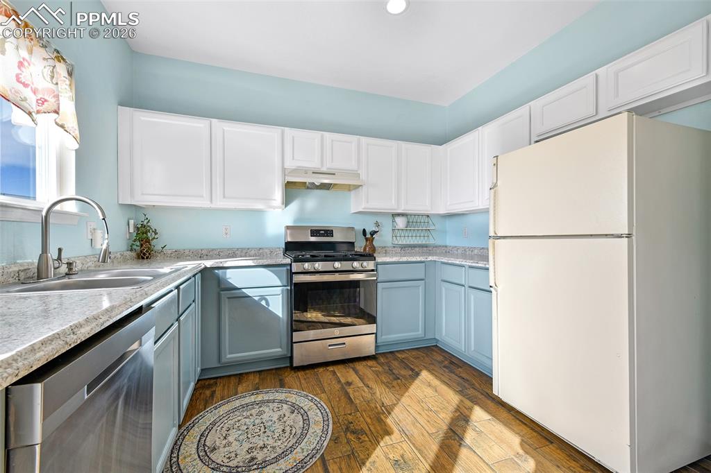 Image 6 of 27: Kitchen with white cabinets, stainless steel appliances, dark wood finished