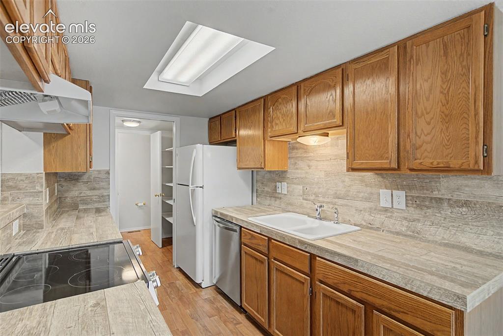 Image 14 of 30: Kitchen featuring wood cabinetry, wood-finish flooring, and a skylight