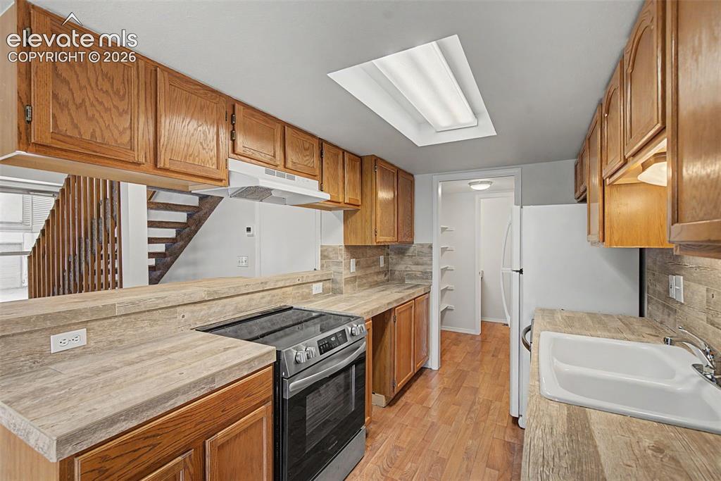 Image 15 of 30: Bright kitchen featuring abundant wood cabinetry, wood-finish flooring, a b