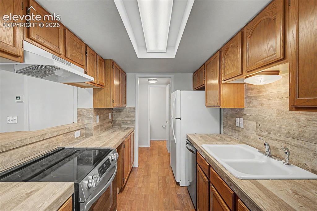 Image 16 of 30: Galley kitchen featuring wood-finish flooring, wood cabinetry, a stainless