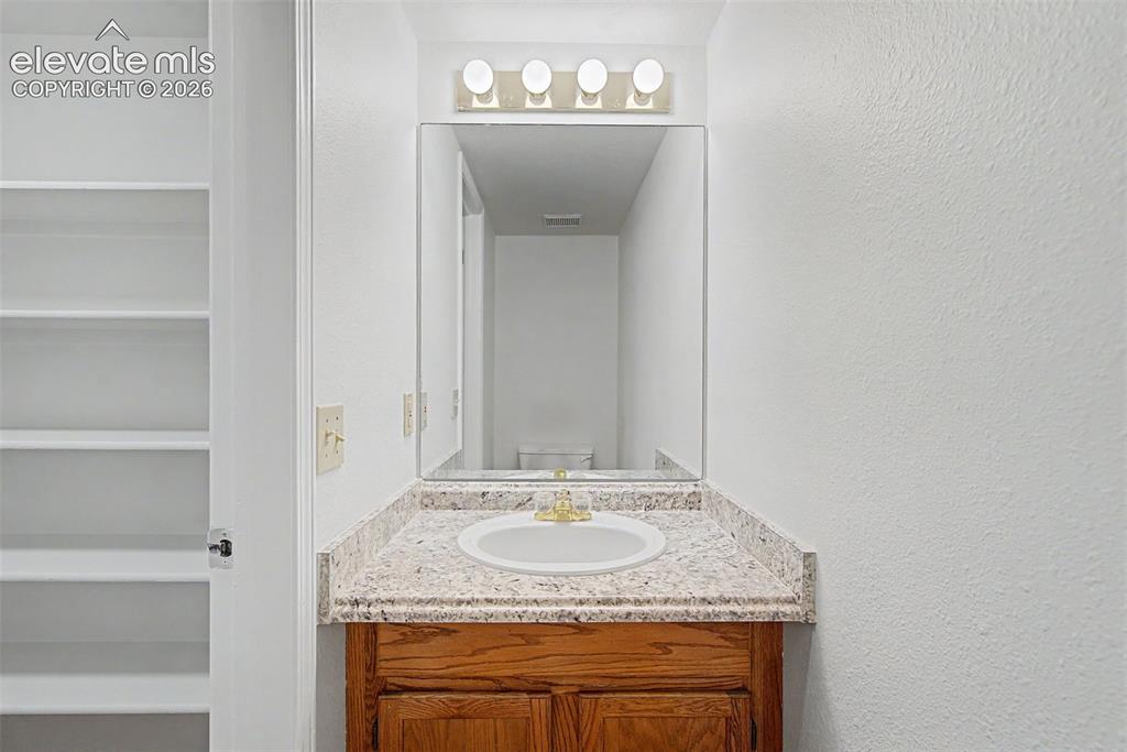 Image 18 of 30: Bathroom vanity featuring a white drop-in sink, gold-toned faucet, and a sp