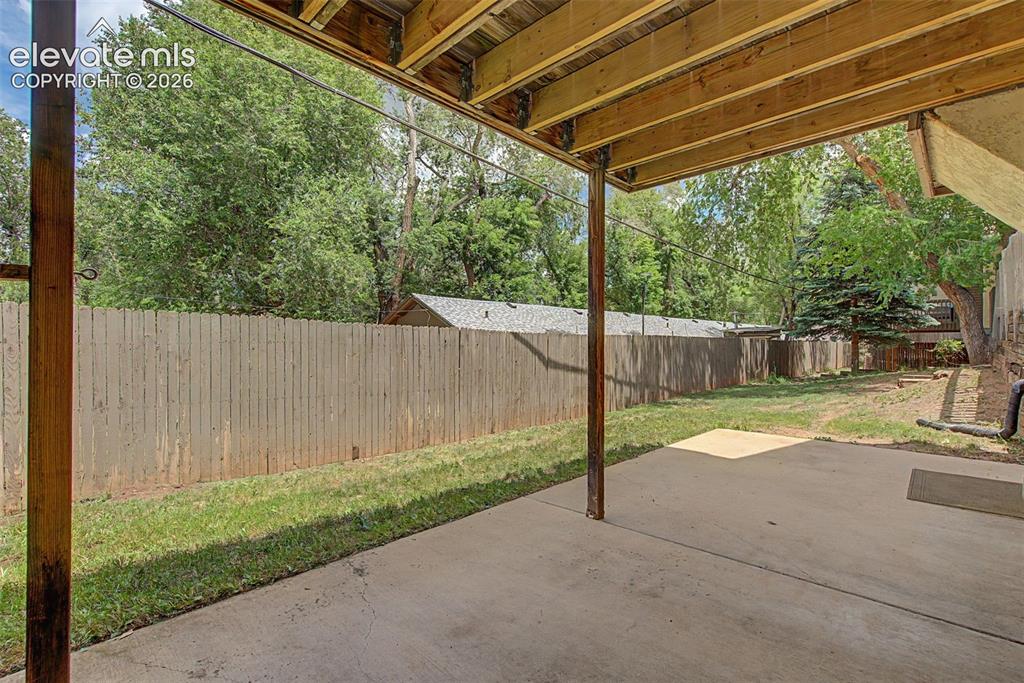 Image 29 of 30: Covered concrete patio with exposed wood joists and support beams, opening