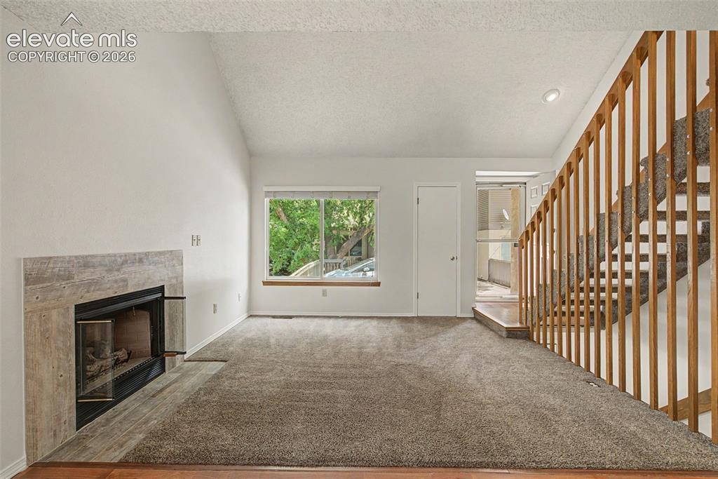 Image 7 of 30: Living area featuring a fireplace with a textured surround, a large window,