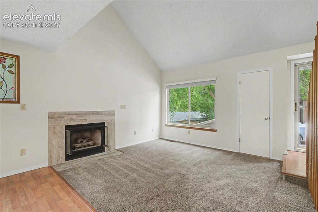 Image 8 of 30: Living room featuring a vaulted ceiling, a fireplace with a light-toned sto