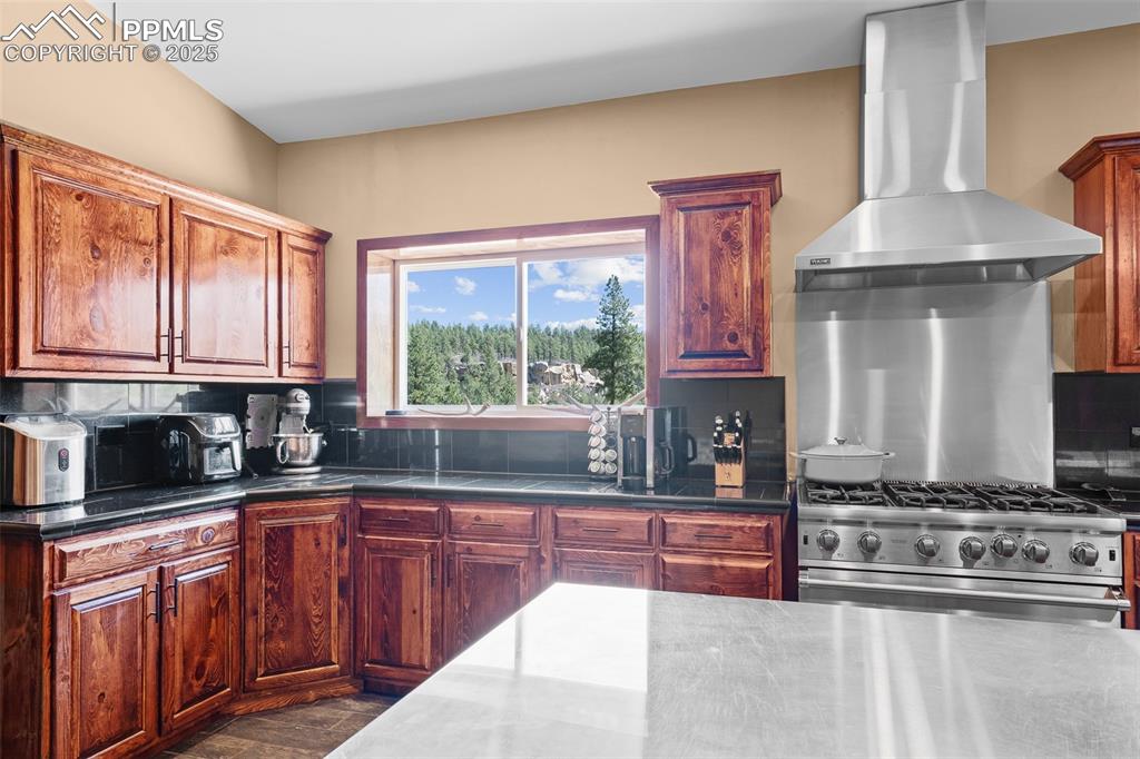 Image 12 of 40: Kitchen featuring wall chimney range hood, backsplash, and stainless steel