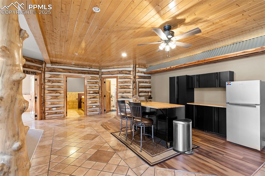 Image 32 of 40: Kitchen featuring rustic walls, wood ceiling, dark cabinets, freestanding r
