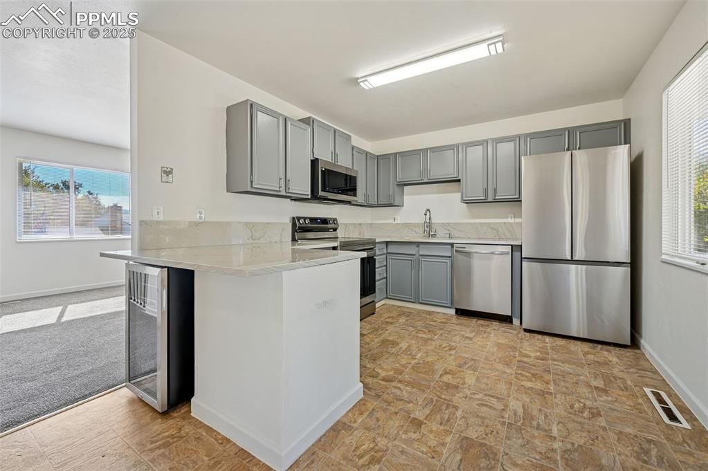 Image 10 of 27: Kitchen with healthy amount of natural light, gray cabinetry, appliances wi