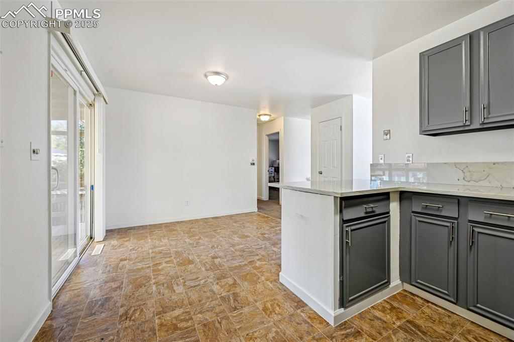Image 11 of 27: Kitchen with gray cabinets, light stone counters, a peninsula, and stone fi