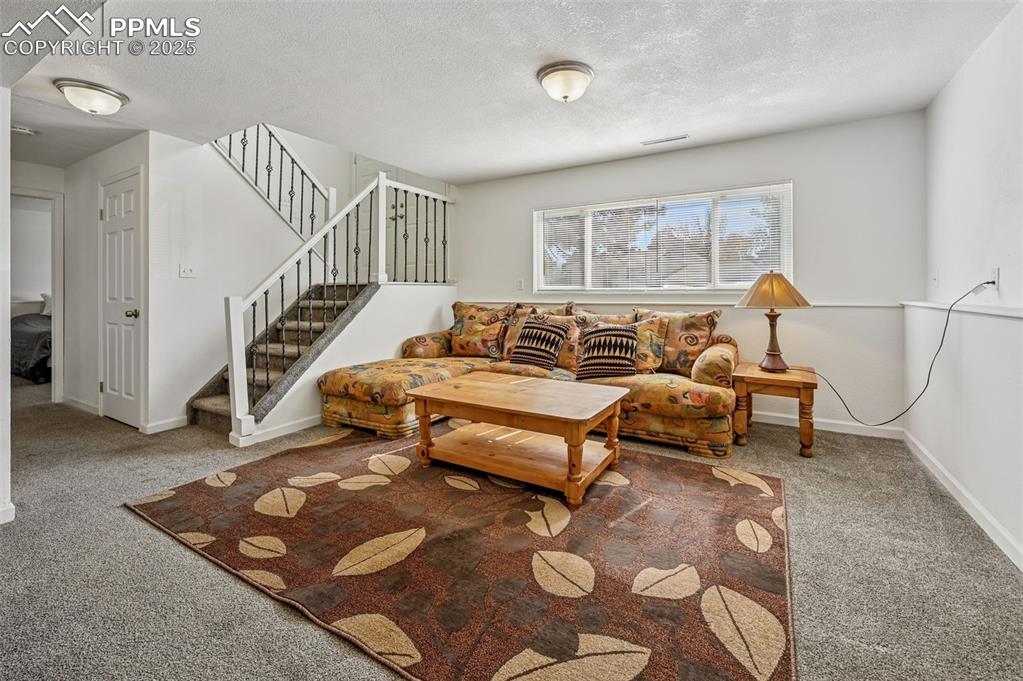 Image 18 of 27: Carpeted living room featuring a textured ceiling and stairway